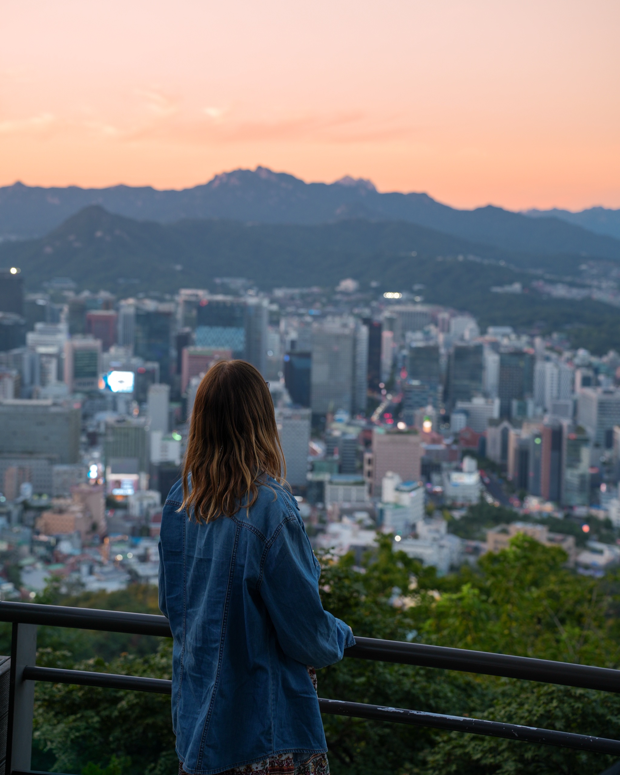 Polina in a denim jacket looking out over Seoul at sunset from Namsan Mountain
