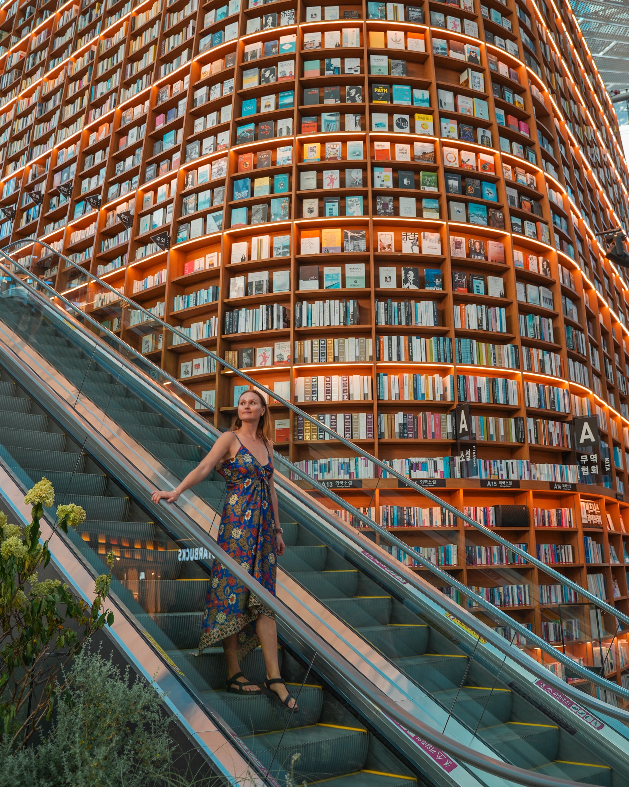 Polina on the escalator beside the towering bookshelves of Starfield Library at COEX