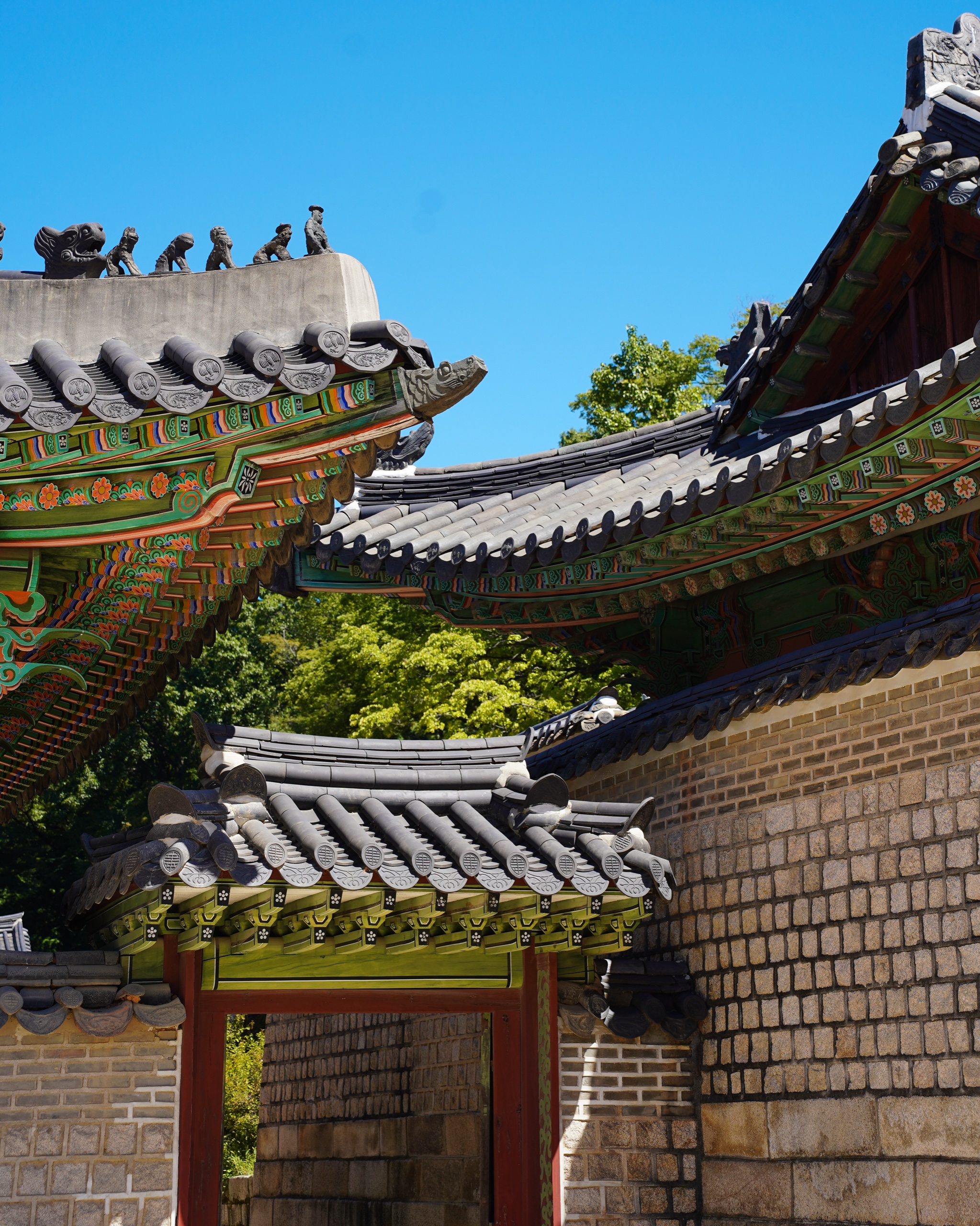 Tiled palace rooftops with painted eaves above a stone wall at Changdeokgung under a blue sky