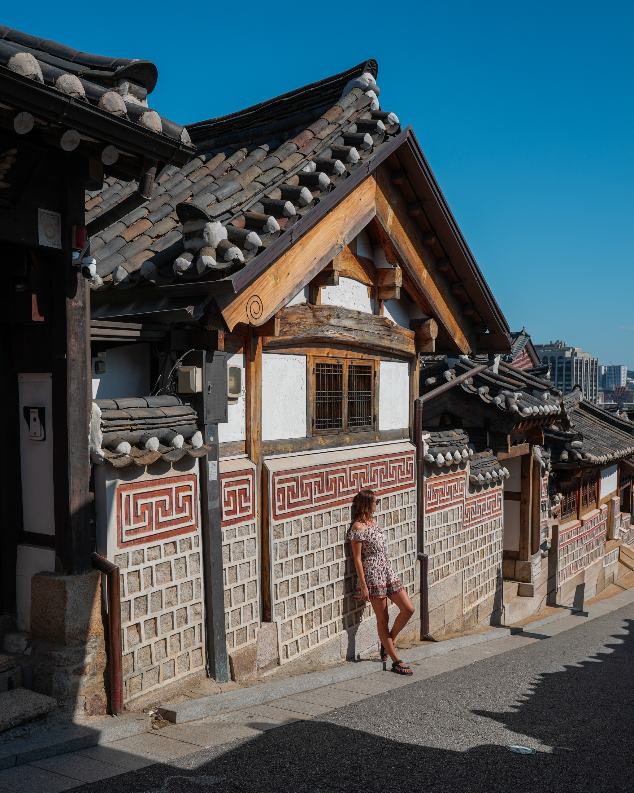 Polina standing beside a hanok house with patterned brick walls on a sunny Bukchon lane