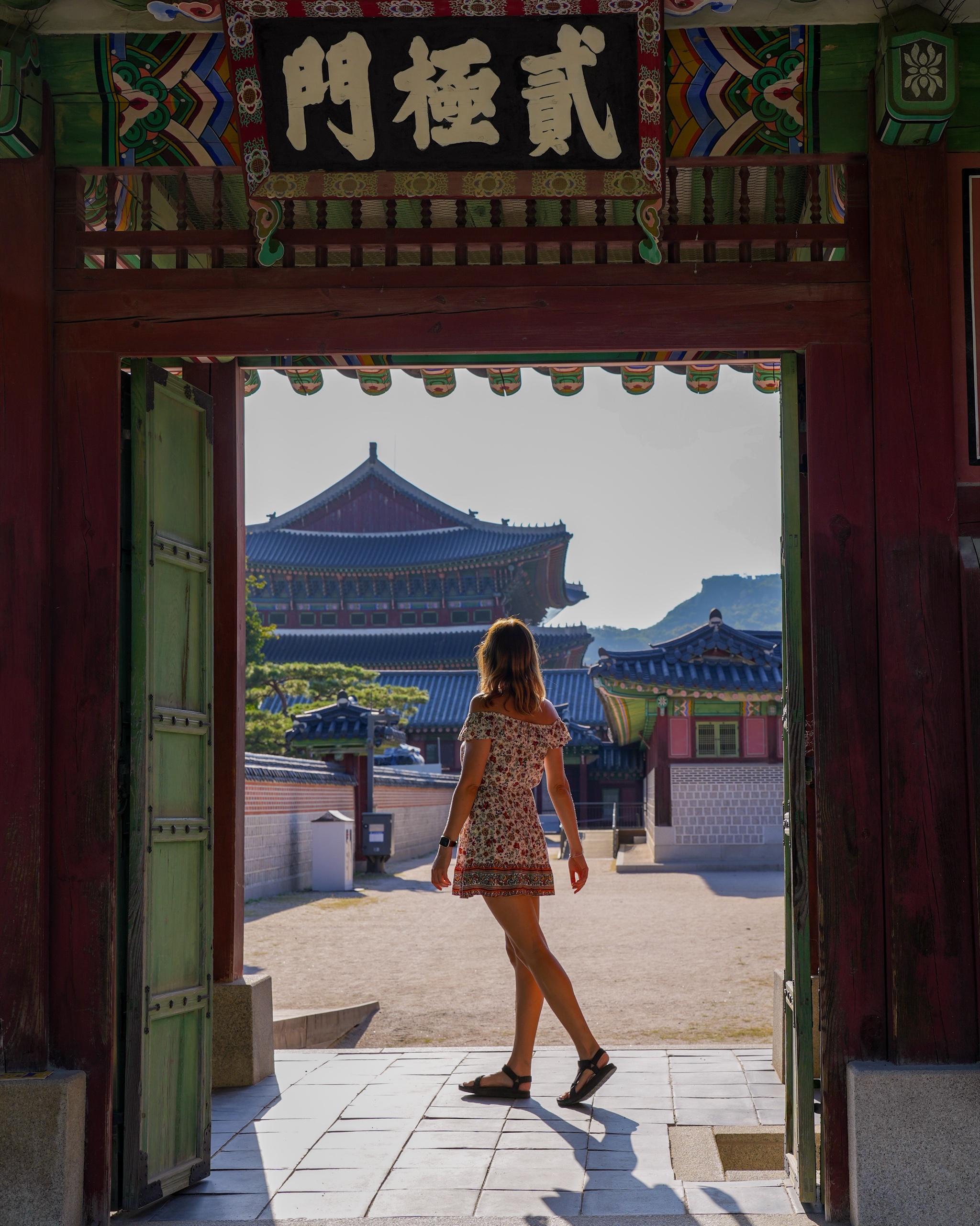 Polina walking through a wooden palace gate toward a hall at Gyeongbokgung