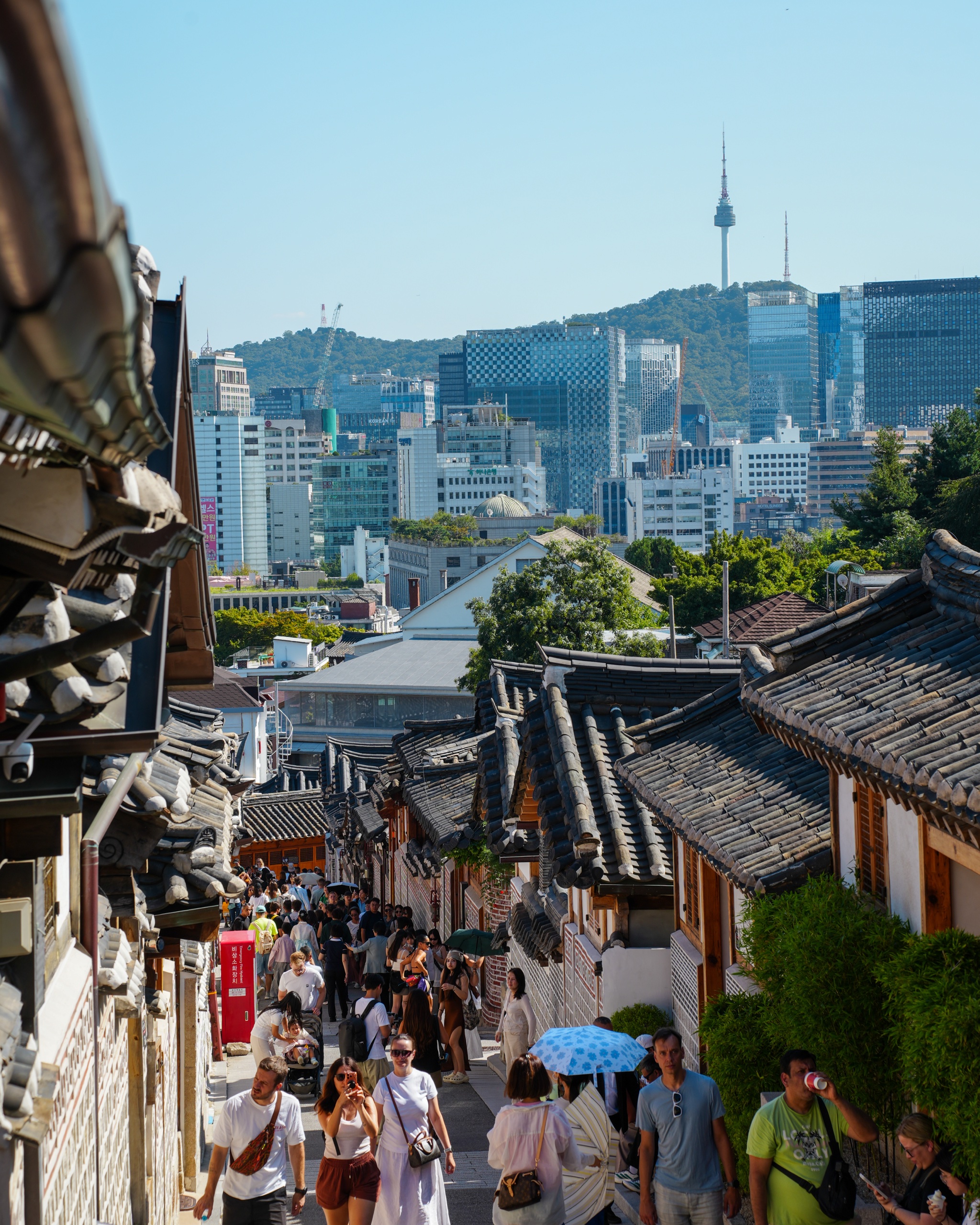 Visitors walking down a Bukchon hanok lane with N Seoul Tower on the skyline