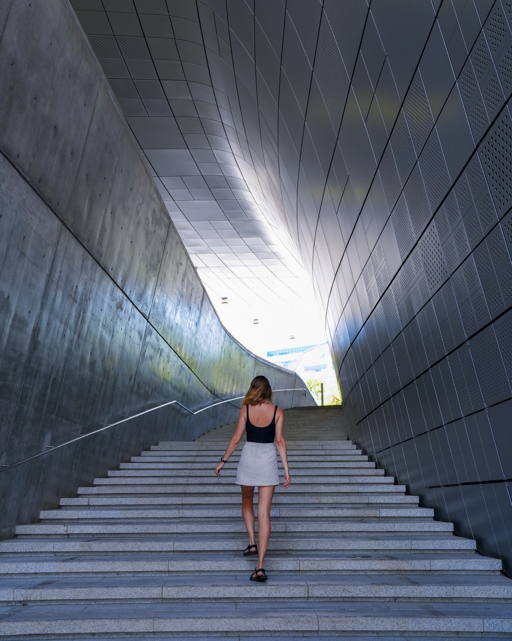 Polina walking up a curved stairway inside Dongdaemun Design Plaza