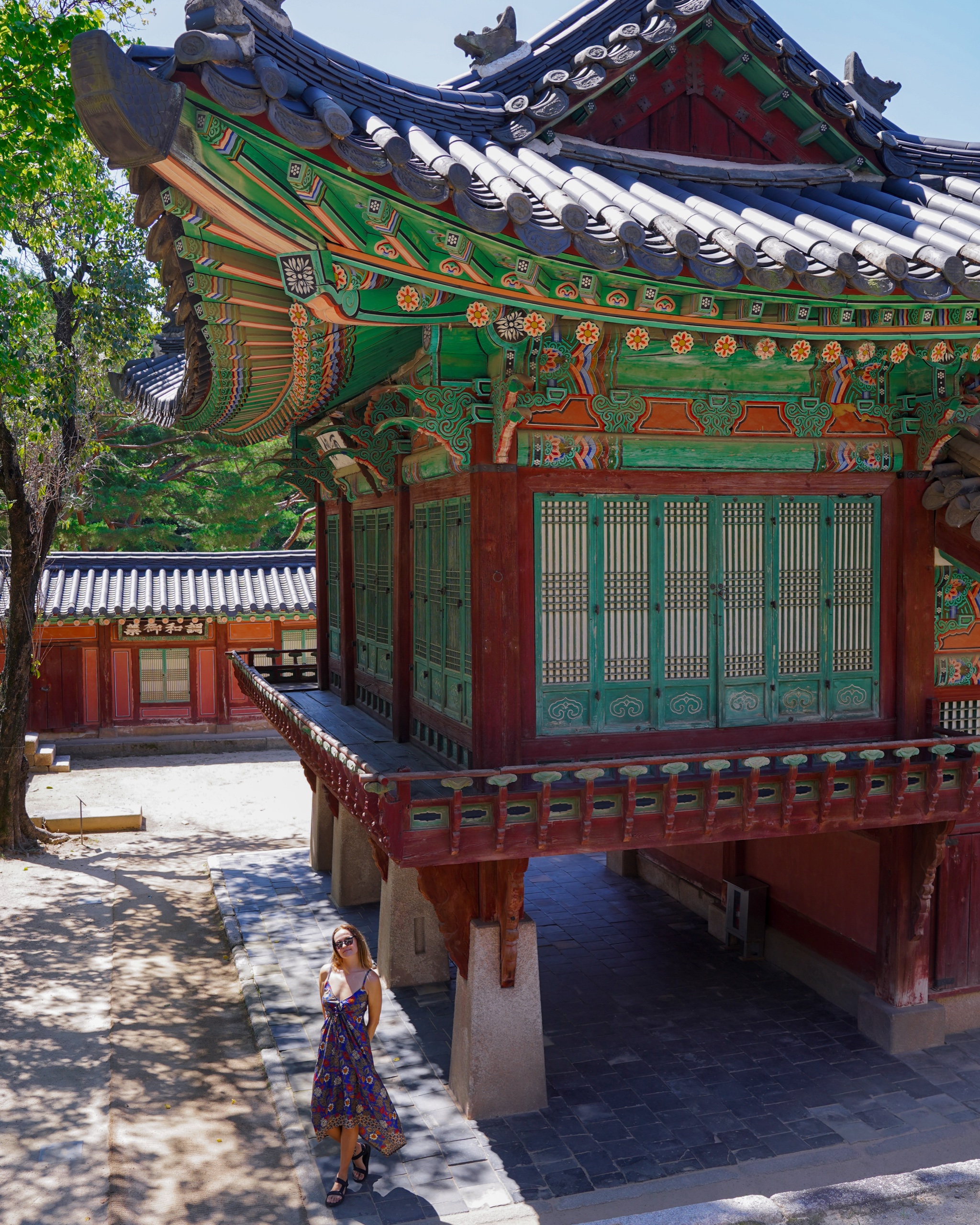 Polina walking beneath a pavilion with green and red painted eaves at Changdeokgung Palace